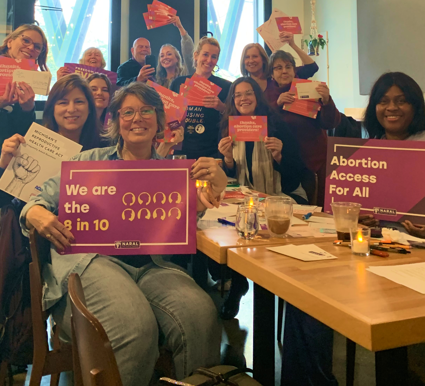 Reproductive Freedom for All members at a postcard party in Michigan, holding up postcards that say, 'Thanks, abortion care providers!' and signs that say, 'We are the 8 in 10' and 'Abortion Access for All.'